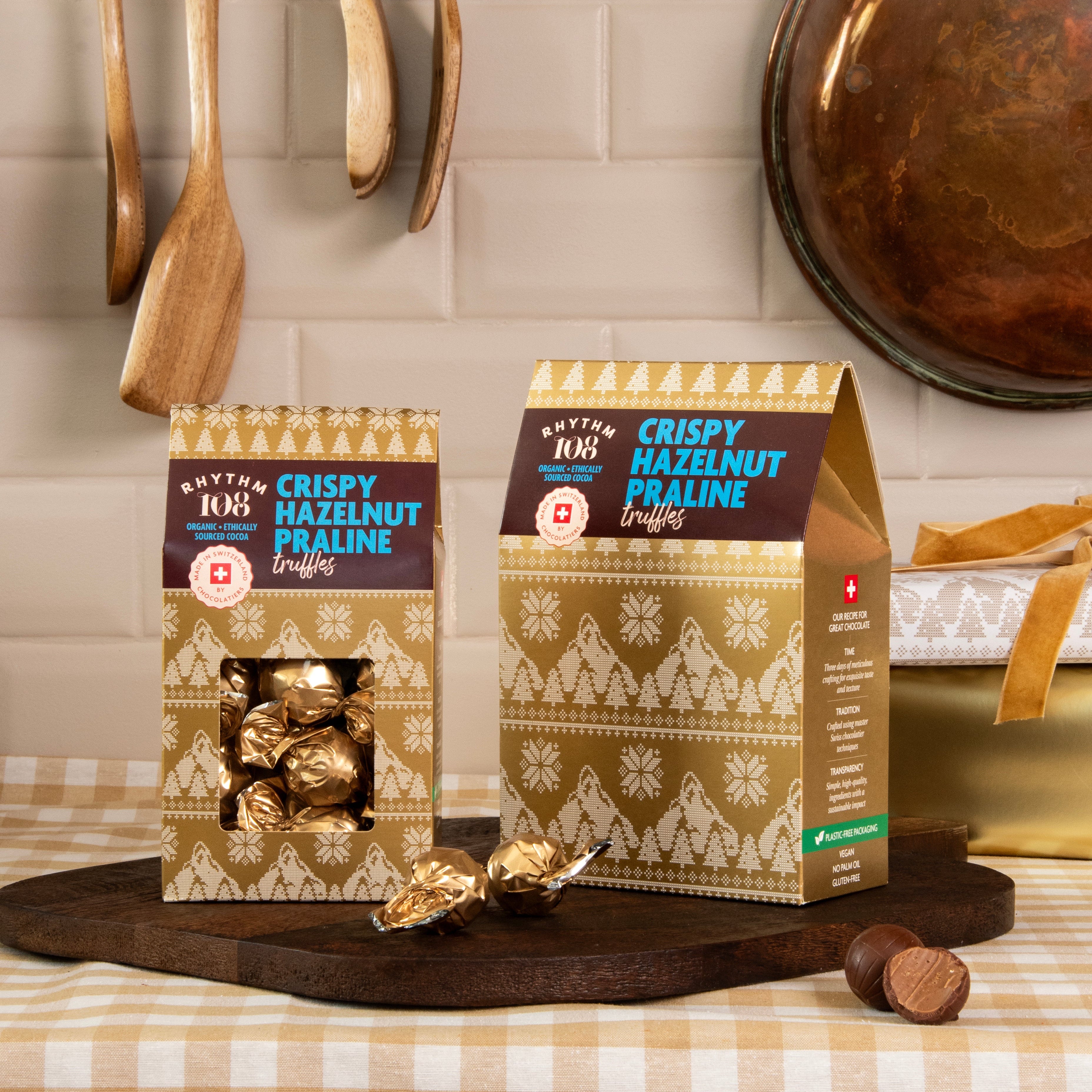 Two boxes of rhythm 108 crispy hazelnut praline truffles on a kitchen counter with utensils in the background.