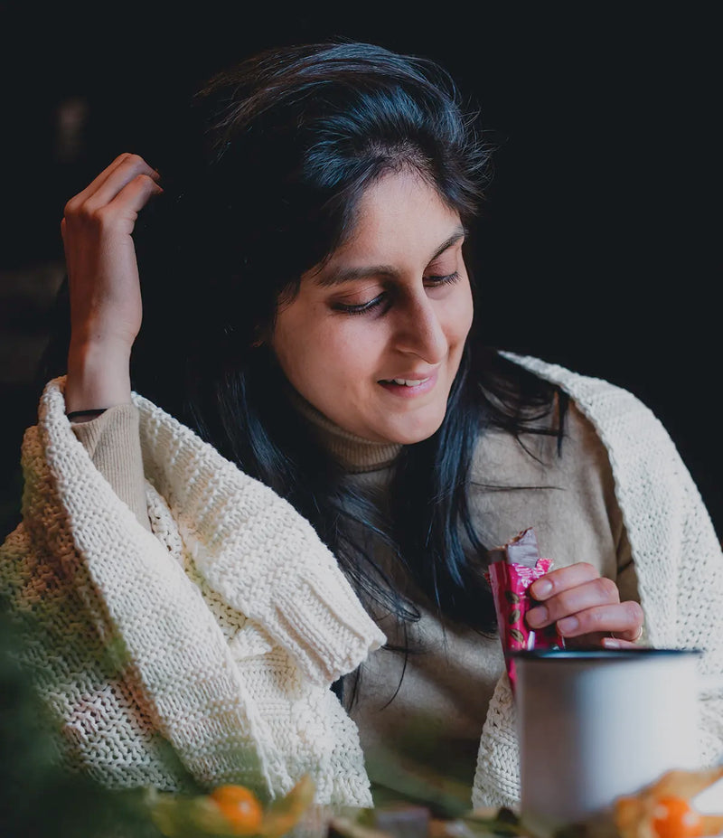 Founder sitting at a table with a warm blanket, holding a Rhythm 108 bar